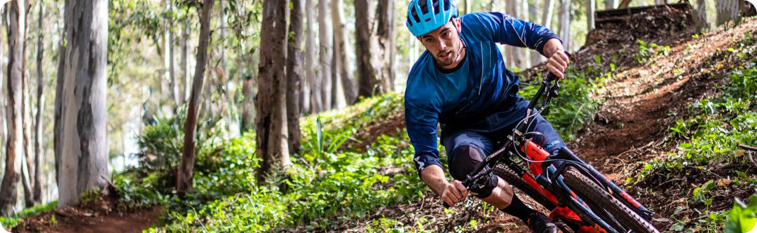 Photo of a young man on a mountain bike riding aggressively on a trail downhill in the forest.