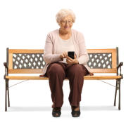 Photo of a senior woman on a white background sitting on a bench. She is smiling while she looks at her phone.